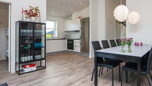 A modern kitchen with a dining area, featuring a wooden floor, white cabinets, and a black dining table with chairs.