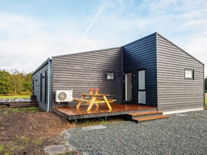 A modern, single-story building with a dark exterior, a wooden deck, and a large air conditioning unit.