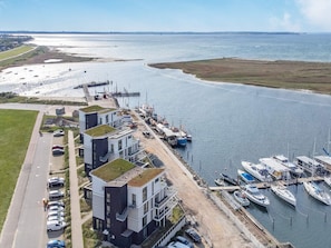 Vue aérienne d’une marina côtière, avec ses bâtiments modernes, son aire de stationnement et ses bateaux amarrés.