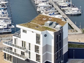 Un bâtiment moderne doté d’un toit plat, de grandes fenêtres et, au fond, d’un port de plaisance.