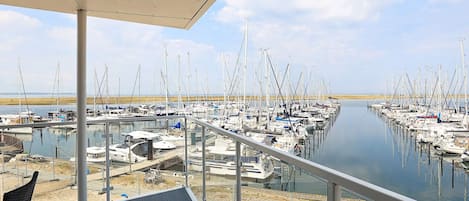 A marina with boats docked in calm waters, a covered area with a railing, and a view of the distant shoreline.