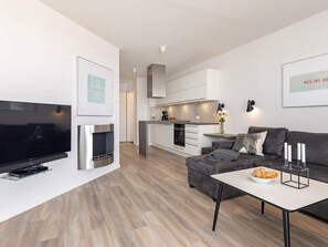 A modern living room with a flat-screen TV, a sofa, a coffee table, and a kitchen in the background. - 5 Star Holiday Home in Wendtorf (Wendtorf)
