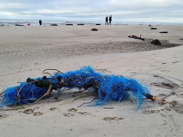 A beach with scattered debris, including blue fishing nets and rocks.
