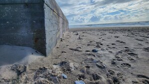 A concrete structure adjacent to a sandy beach with visible footprints and a partly cloudy sky.