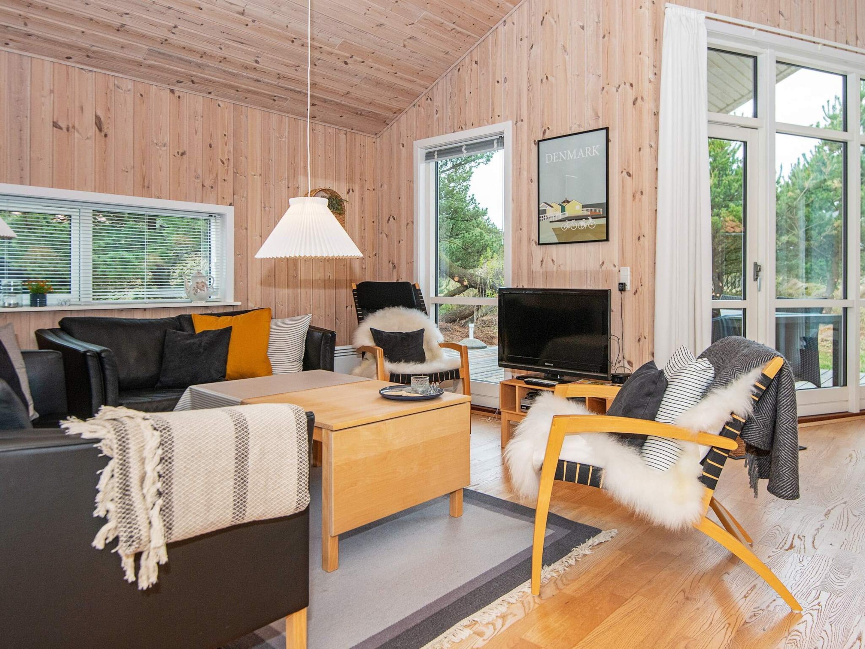 En moderne stue med sofa, stole, fjernsyn og et stort vindue.