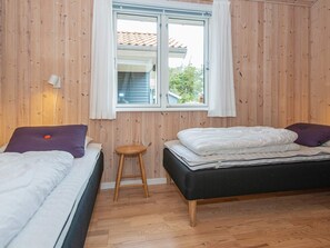 A room with two beds, a window, wooden walls, and a wooden stool.