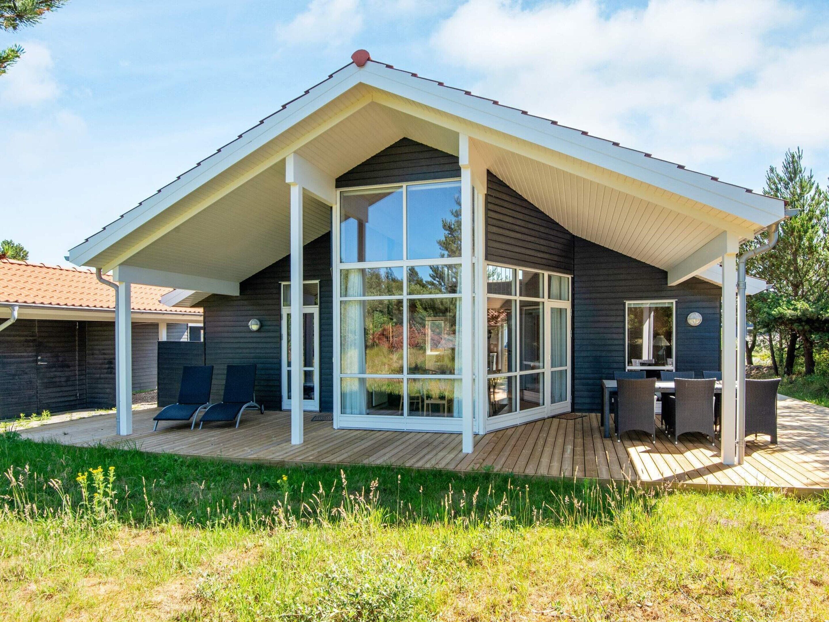 Ein modernes Haus mit großen Glasfenstern, einer überdachten Terrasse und einer Holzterrasse.