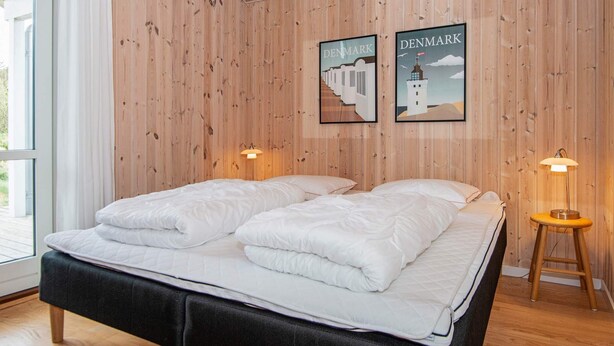 A double bed with a black headboard in a room with wooden walls and two framed pictures of Denmark.