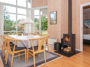 A cozy room with a dining table, chairs, a wood-burning stove, and a bed. - 4 Star Holiday Home in Ulfborg (Ulfborg)