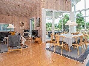 A cozy room with wooden walls and floors, a dining area with a table and chairs, a sofa, a chair, and a television on a stand. - 4 Star Holiday Home in Ulfborg (Ulfborg)