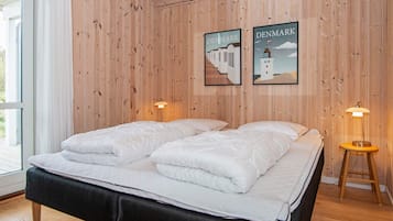 A double bed with a black headboard in a room with wooden walls and two framed pictures of Denmark.