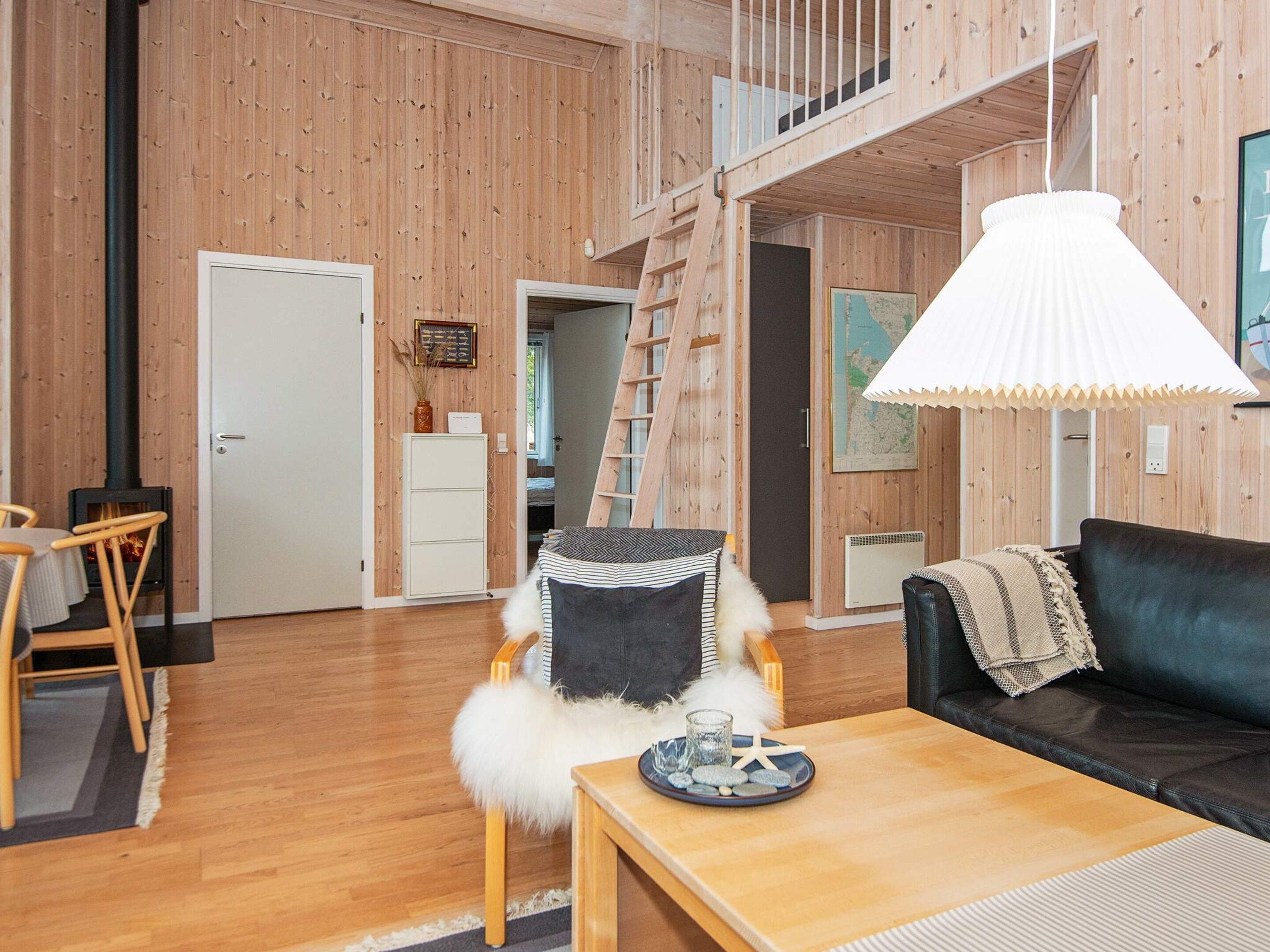 A cozy cabin interior with a wooden interior, a loft bedroom, a dining area, and a fireplace.