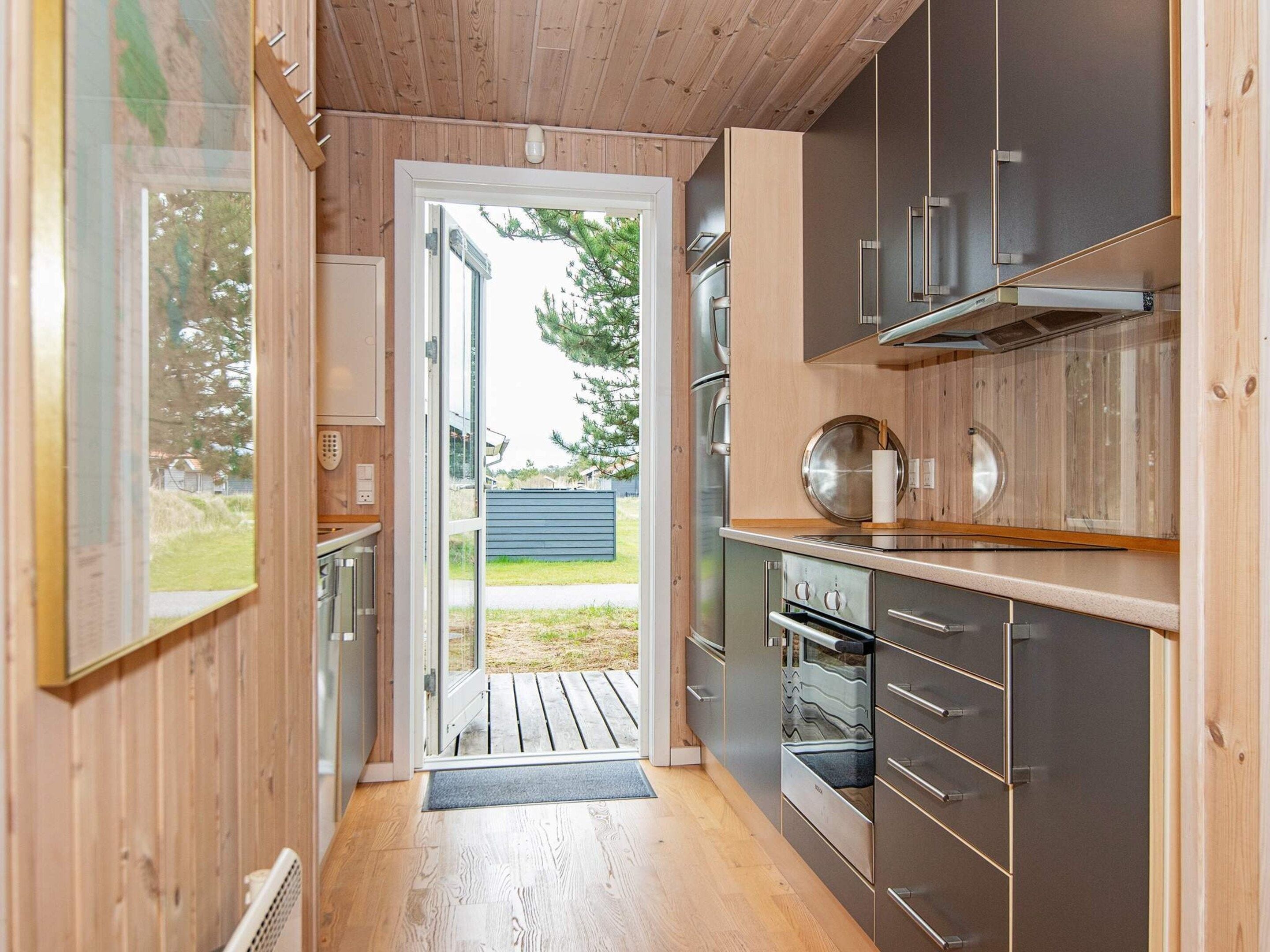 A modern kitchen with wooden walls, stainless steel appliances, and a view through the door.