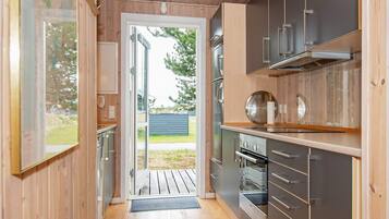A modern kitchen with wooden walls, stainless steel appliances, and a view through the door.