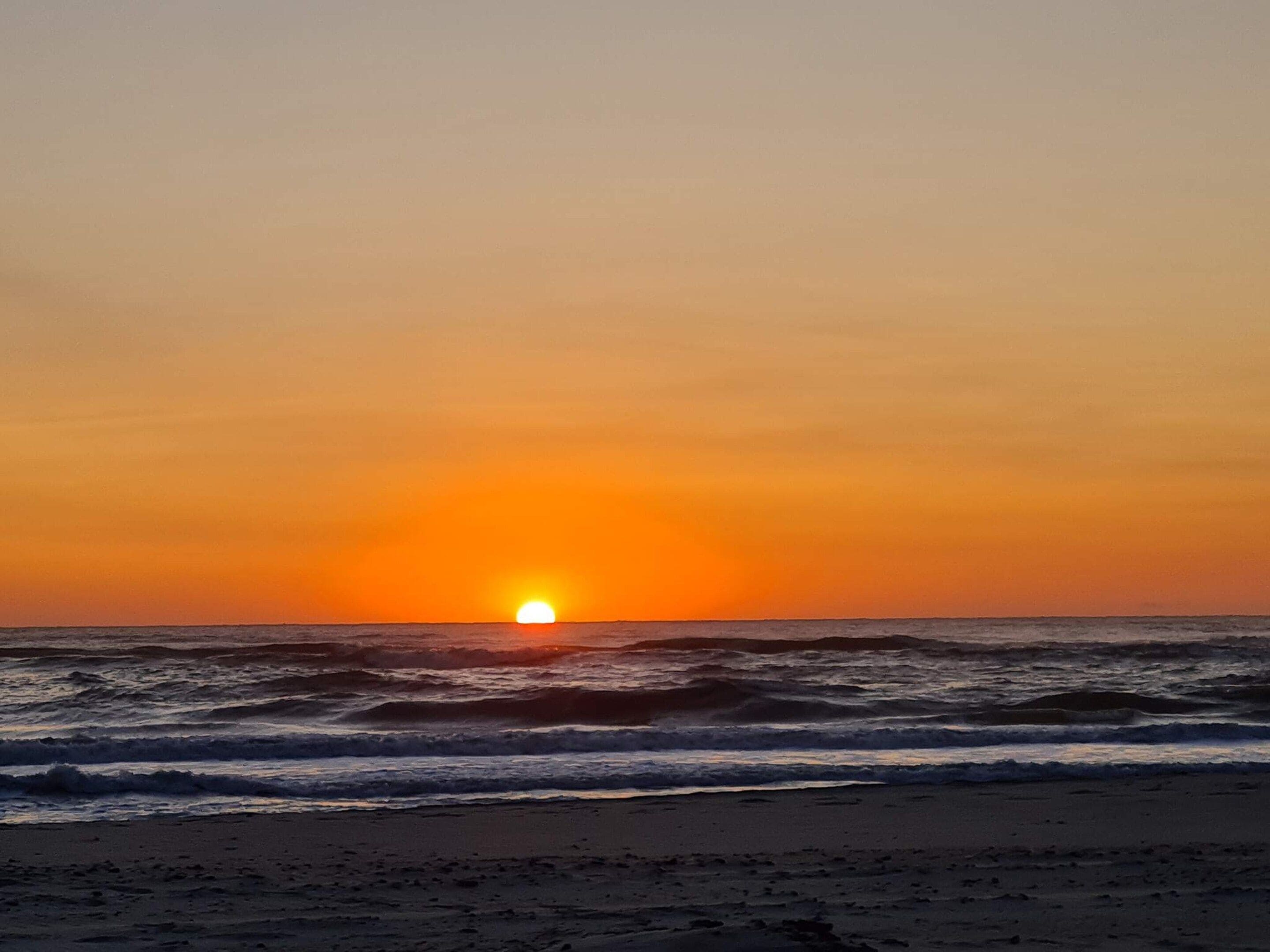 A sunset over the ocean with waves approaching the shore.