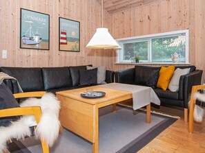 A cozy living room with a wooden interior, a black leather sofa, a wooden coffee table, and two framed pictures on the wall.