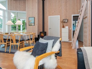 A cozy room with wooden walls, a fireplace, a dining area with a table and chairs, and a view of greenery outside.