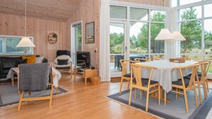 A cozy room with wooden walls and floors, a dining area with a table and chairs, a sofa, a chair, and a television on a stand.