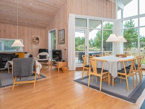 A cozy room with wooden walls and floors, a dining area with a table and chairs, a sofa, a chair, and a television on a stand.