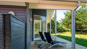 A wooden deck with a covered area, a sliding glass door, and two lounge chairs.