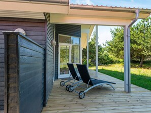 A wooden deck with a covered area, a sliding glass door, and two lounge chairs.