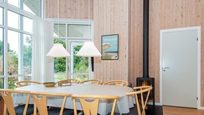 A dining area with a round table, wooden chairs, and a view of greenery outside.