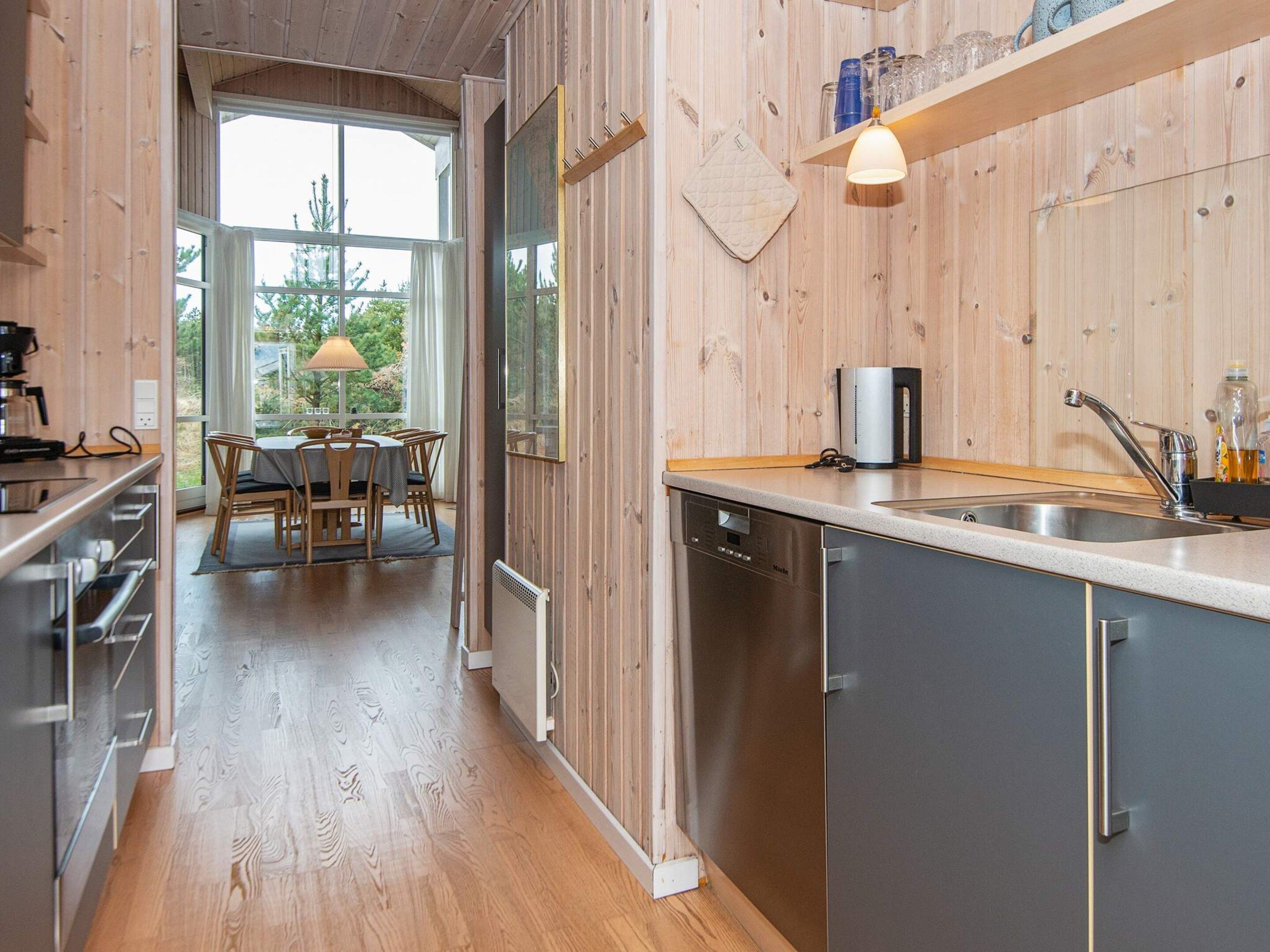 Una cucina moderna con rivestimenti in legno, lavastoviglie, lavello e zona pranzo con tavolo e sedie.