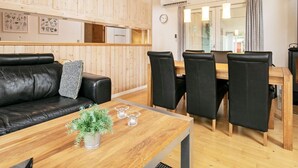 Een modern interieur met een houten plafond, een eethoek met een houten tafel en stoelen, een zwarte leren bank en een kleine plant op de tafel.
