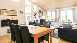 Een moderne woonkamer met een houten eettafel, zwarte leren stoelen, een zwarte bank en een groot raam met gordijnen.