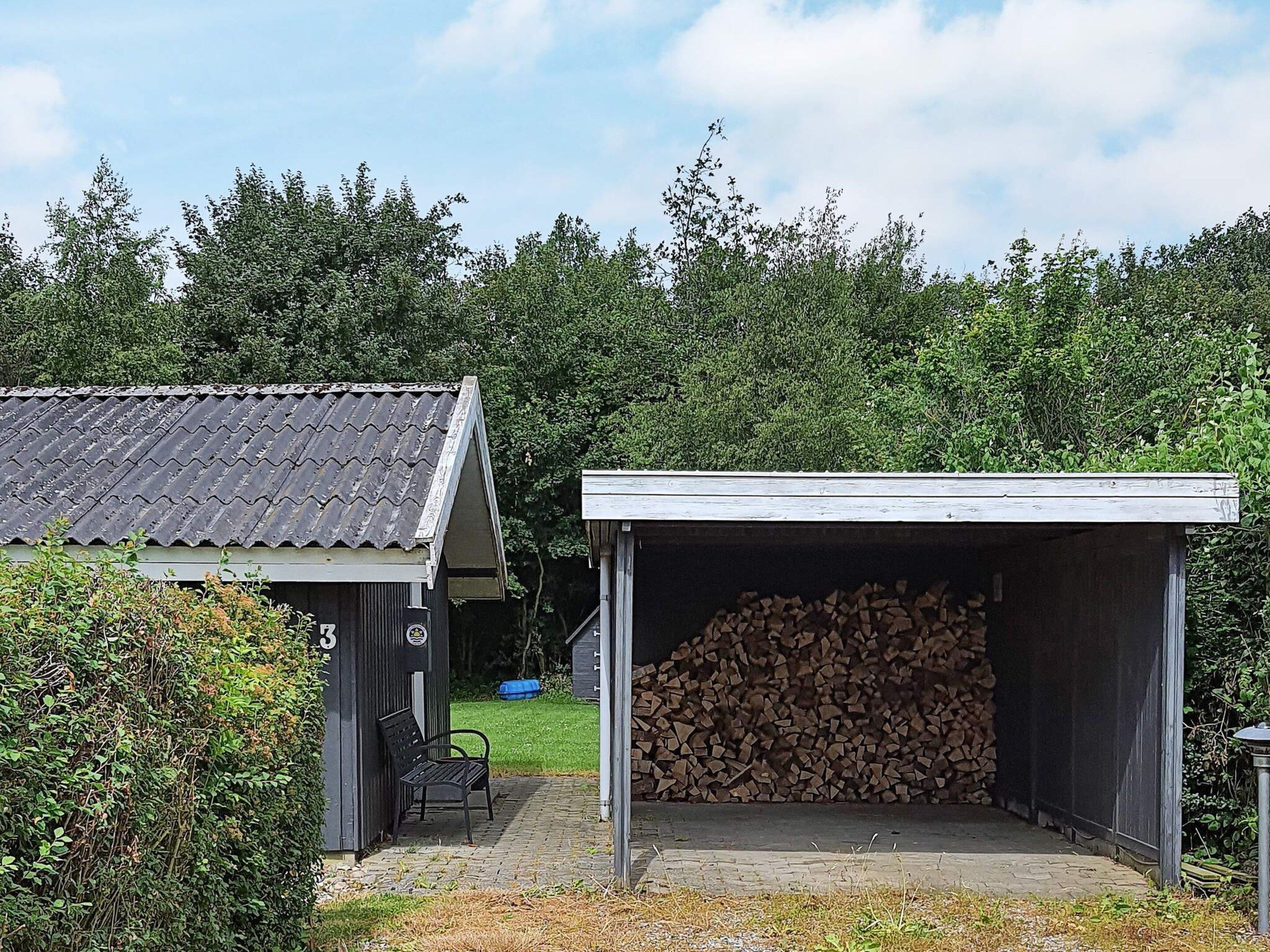 A building with a covered outdoor area, a bench, and a pile of firewood.