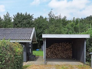 Un bâtiment doté d’un espace extérieur abrité, d’un banc et d’une pile de bois de chauffage.