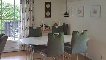 A dining area with a round table, four chairs, a hanging light fixture, and a window with curtains.