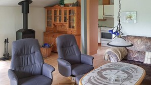 A living room with two armchairs, a coffee table, a sofa, a wooden cabinet, a fireplace, and a kitchen area. - 6 Person Holiday Home in Sydals (Sydals)