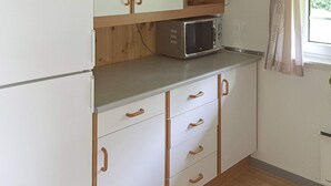 A compact kitchen with white cabinets, a microwave, and a window with curtains. - 6 Person Holiday Home in Sydals (Sydals)