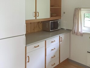 A compact kitchen with white cabinets, a microwave, and a window with curtains. - 6 Person Holiday Home in Sydals (Sydals)