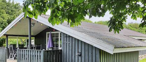 A wooden cabin with a porch, a covered seating area, and a window.
