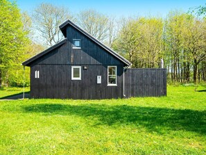 A dark wooden building with a sloped roof, a small window, and a door. - 6 Person Holiday Home in Hovborg (Hovborg)
