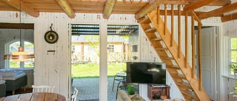 A rustic interior with a wooden staircase, a dining area with a round table and chairs, a sofa, and a television.