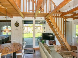 Un interior rústico con una escalera de madera, un comedor con una mesa redonda y sillas, un sofá y un televisor.