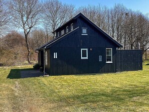 A large, dark wooden building with a gabled roof, a small porch, and a grassy yard. - 6 Person Holiday Home in Hovborg (Hovborg)