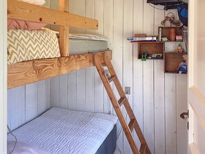 Uma cama beliche com escada de madeira, um pequeno nicho com livros e brinquedos, e uma parede branca com painéis verticais.