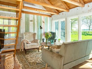 A cozy room with a wooden ceiling, a sofa, a chair, a small table, and a view of greenery outside. - 6 Person Holiday Home in Hovborg (Hovborg)