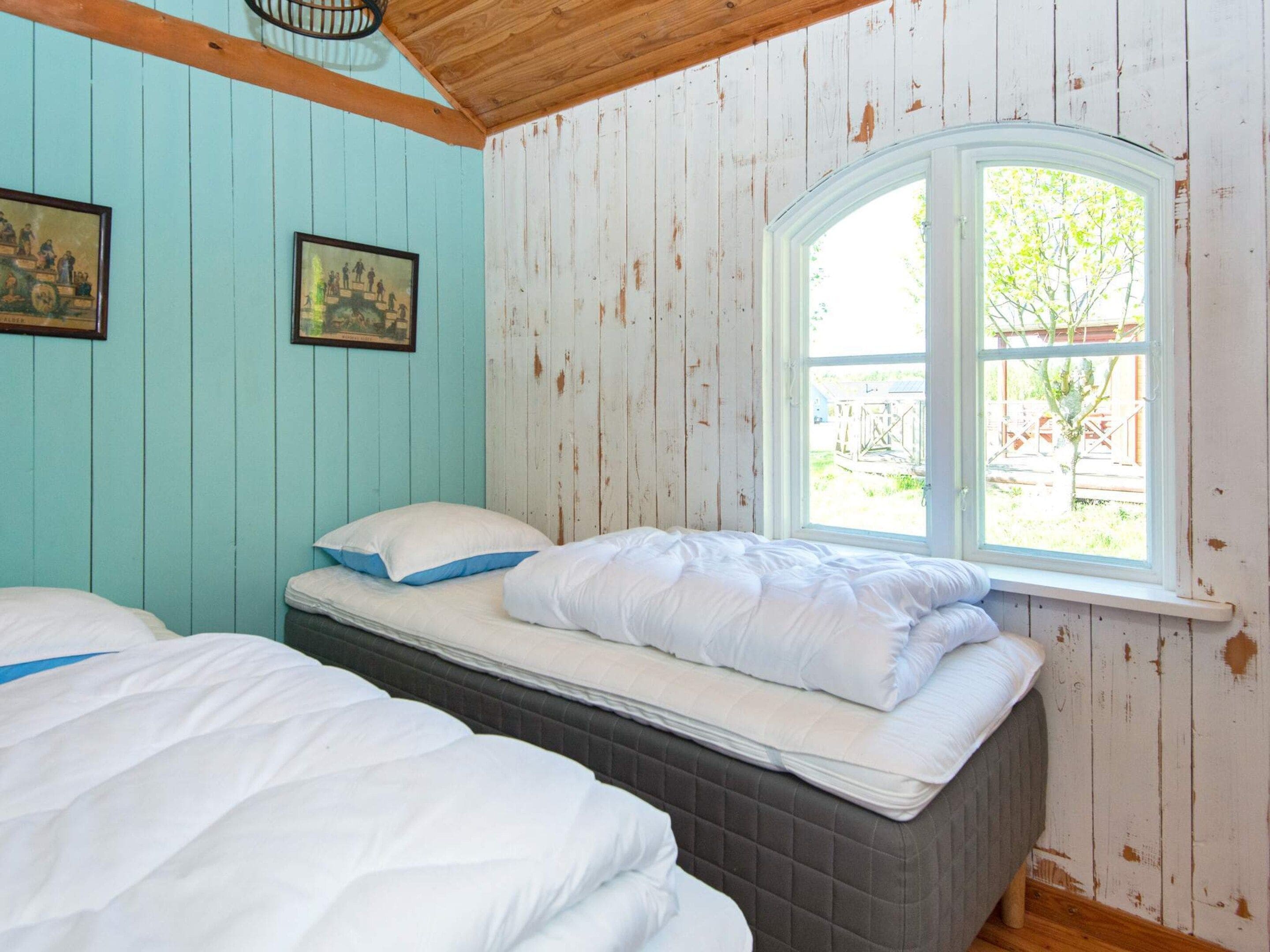 Ein Zimmer mit zwei Betten, einem Fenster mit Blick auf Grünflächen und zwei gerahmten Bildern an der Wand.