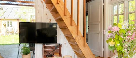 A wooden staircase leading to a room with a flat-screen TV, wicker baskets, and a vase with flowers.
