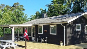 Une petite maison noire avec une terrasse en bois, un drapeau et une table.