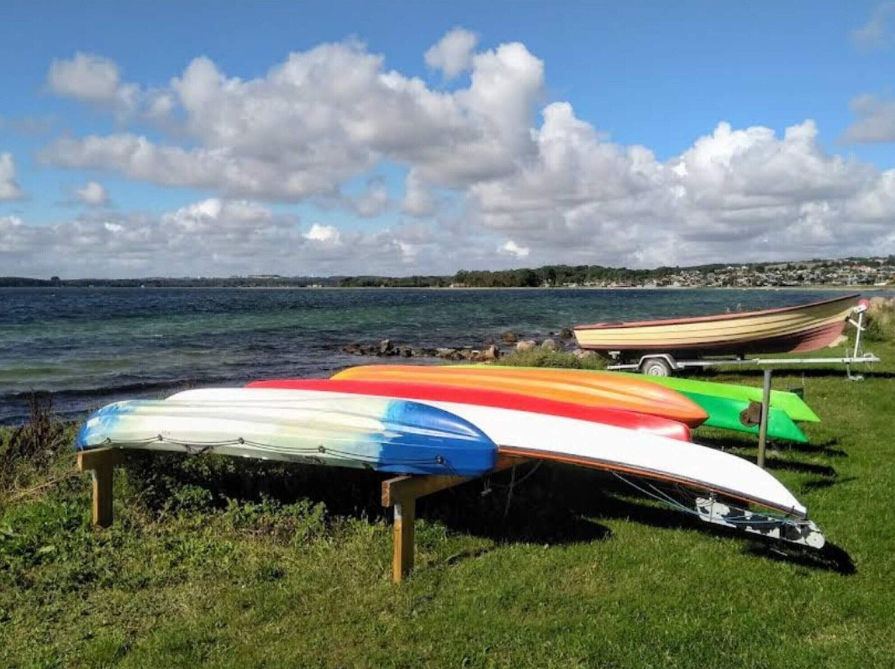 Een grasveld met meerdere kleurrijke boten op een rij, een caravan en uitzicht op zee en de verre kustlijn.