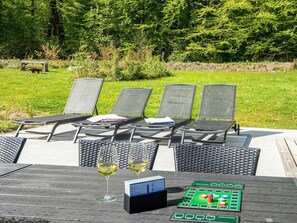 An outdoor seating area with lounge chairs and a table, a wine glass, and a board game.