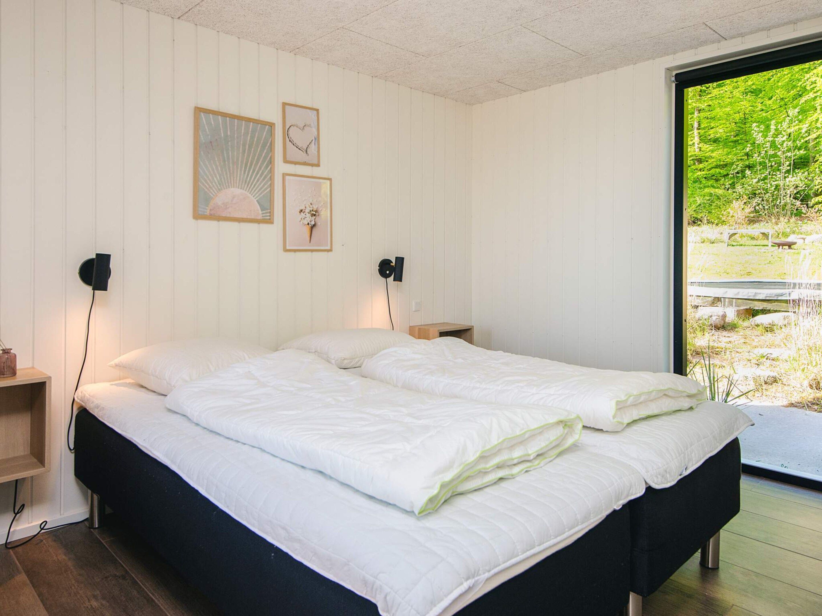 Quarto com uma cama grande, duas mesas de cabeceira e vista para um jardim através de uma porta de correr.