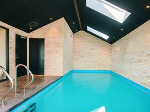 An indoor swimming pool with a skylight, a door, and a metal handrail.