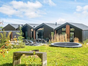 A modern outdoor area with a dining table and chairs, a trampoline, and a wooden structure. - 5 Star Holiday Home in Sjolund (Sjølund)